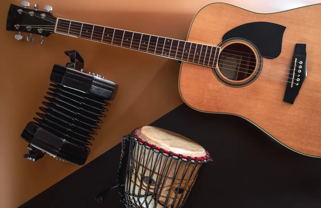 Violão acústico, concertina preta e tambor djembe de madeira sobre fundo geométrico marrom e preto.